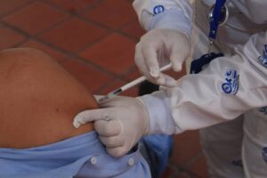 Healthcare worker in protective gear giving a vaccine injection to a patient indoors.