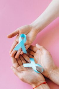 Two hands holding blue awareness ribbons on a pink background, symbolizing support and awareness.